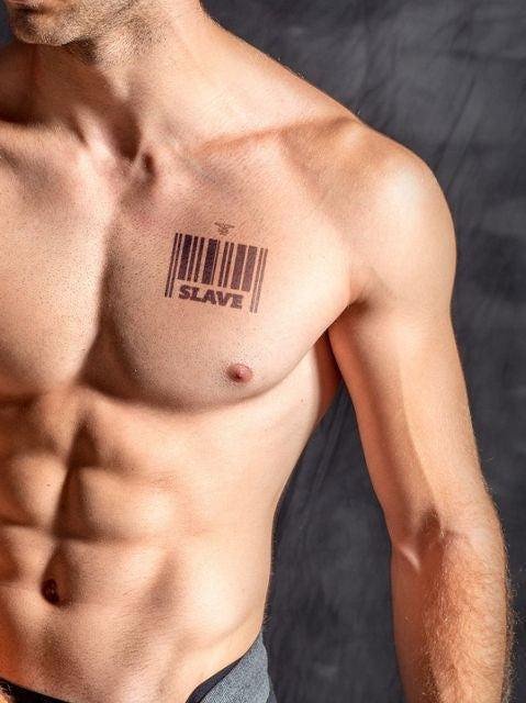 ansicht einer glatten muskolösen männerbrust vor einer dunklen wand der ein temporäres tattoo von mister b auf der linken brust mit einem barcode und der aufschrift slave trägt.