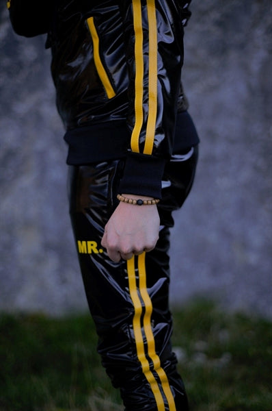 MR Riegillio PVC Tracksuit Hose mit gelben streifen von einem jungen gay getragen in schwarz glänzend mit weissen nike tn sneakern von der seite in nahaufnahme