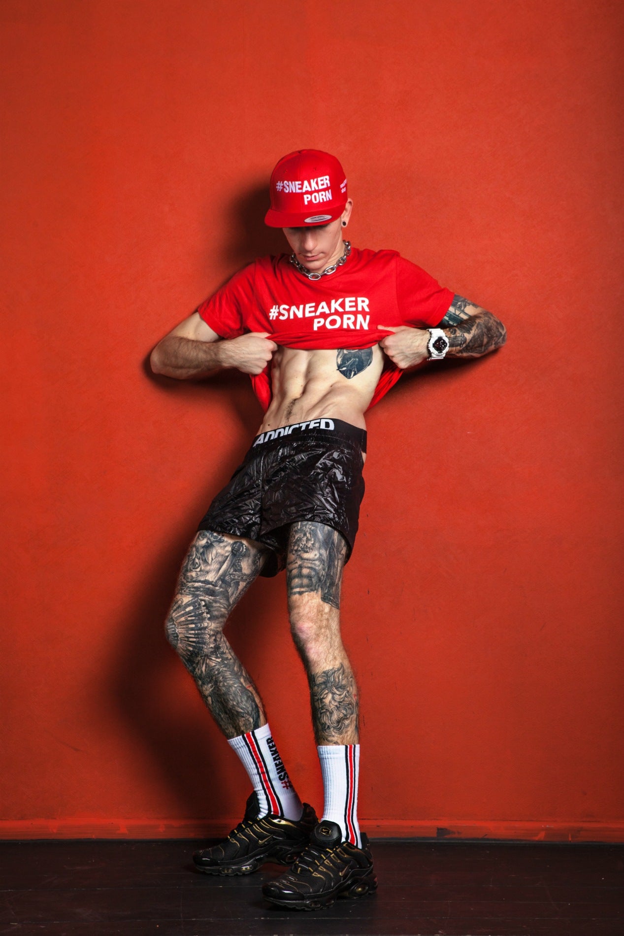 junge mit tattoos und rotem t-shirt trägt seine addicted jock unterwäsche und pvc-short mit seinen nike tn sneaker und sneakerporn socken in weiss und feuerrot von sk8erboy