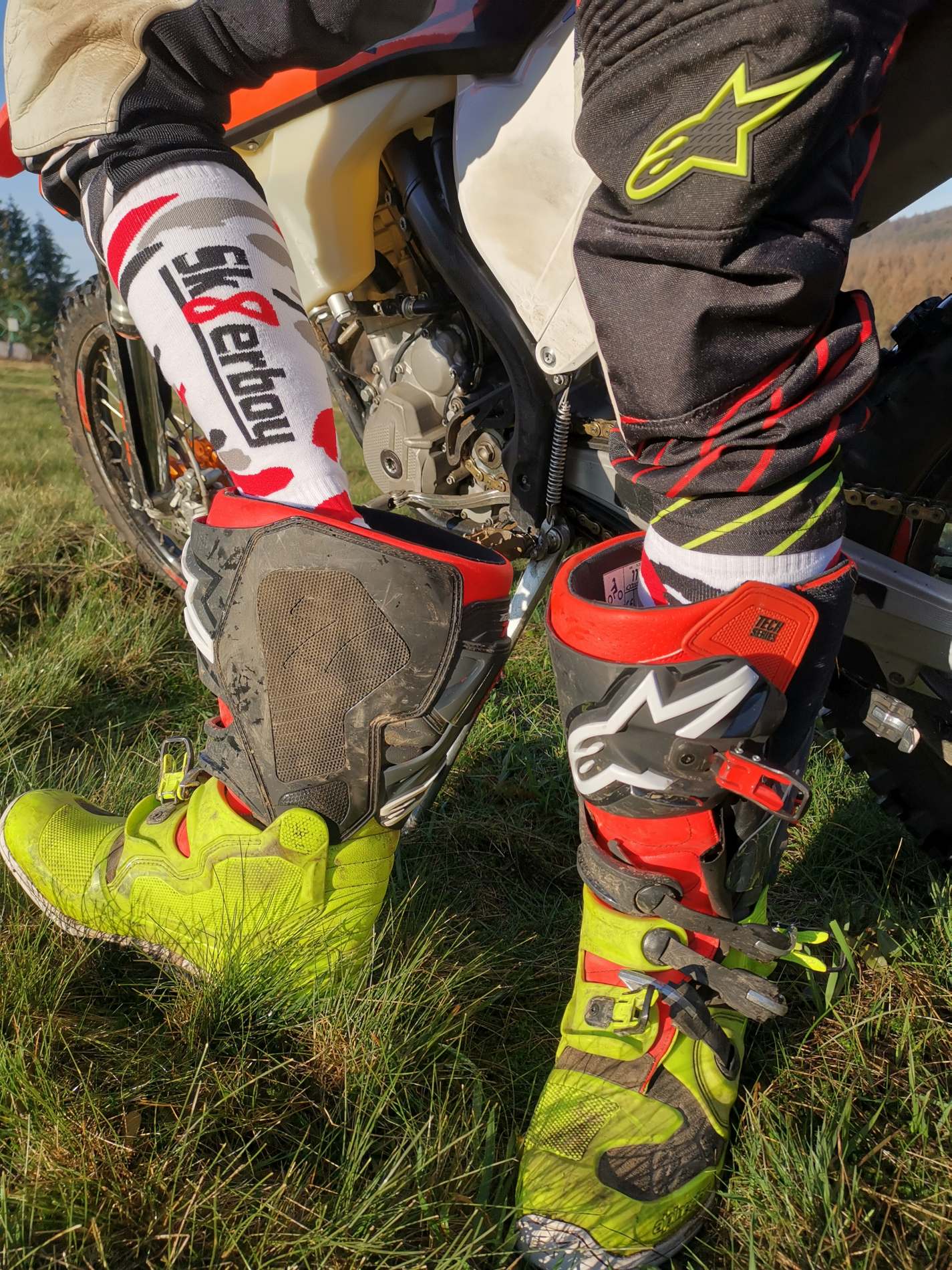 motorradfahrer zieht gerade in der sonne seine stiefel aus und traegt mx socks von sk8erboy in flecktarn muster mit großem logo auf der rueckseite