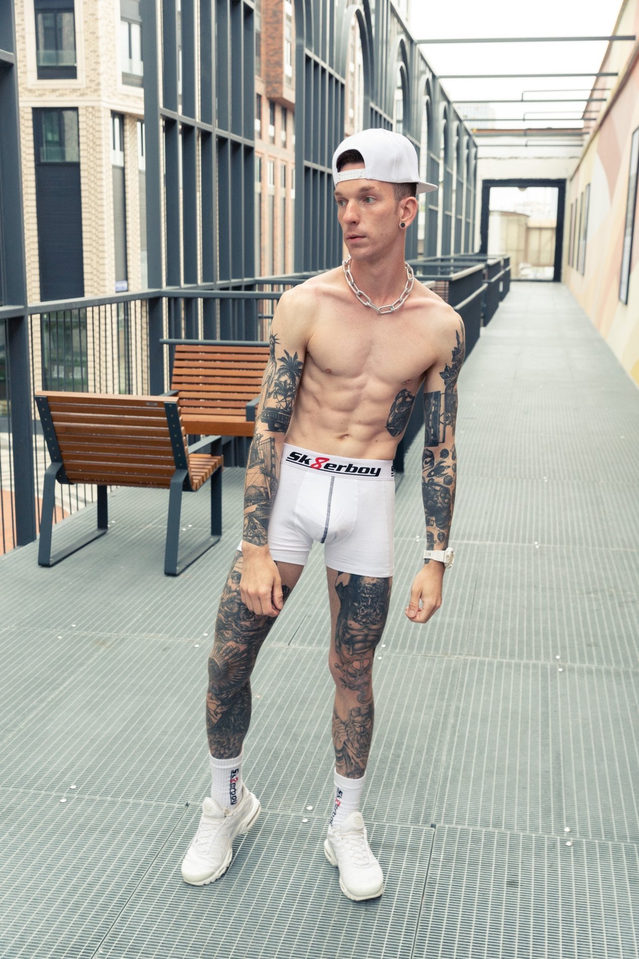 trainierter junge mit freien oberkörper und tattoos auf beinen und armen trägt eine weisse boxershort von sk8erboy mit passenden crew socks in weiss und nike tn sneaker mit kappe und stahlkette um den hals.